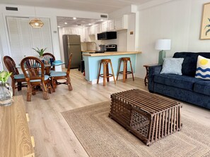 A modern kitchen with white cabinets, a central island with stools, and a dining area with wooden chairs. - Oceanside Condo - Sleeps 6 - Beach Gear - Parking (Ocean City)