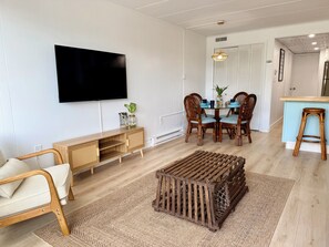 Een woonkamer met een televisie, houten meubels, een eettafel met stoelen en een keukenhoek.