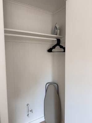 A closet with a hanging rack, an ironing board, and a shelf with a small appliance. - Oceanside Condo - Sleeps 6 - Beach Gear - Parking (Ocean City)