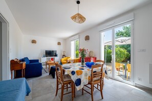 A spacious living area with a dining table, chairs, a sofa, and a television. - Guilvin - Charmante maison à 2 pas du port (Locmariaquer)