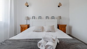 A neatly made bed with white linens, two bedside lamps, and a set of framed pictures on the headboard. - Guilvin - Charmante maison à 2 pas du port (Locmariaquer)