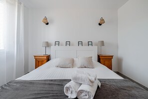 A neatly made bed with white linens, two bedside lamps, and a set of framed pictures on the headboard. - Guilvin - Charmante maison à 2 pas du port (Locmariaquer)