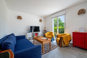 A living room with a sofa, a coffee table, a TV, a yellow chair, a red cabinet, and a large window. - Guilvin - Charmante maison à 2 pas du port (Locmariaquer)