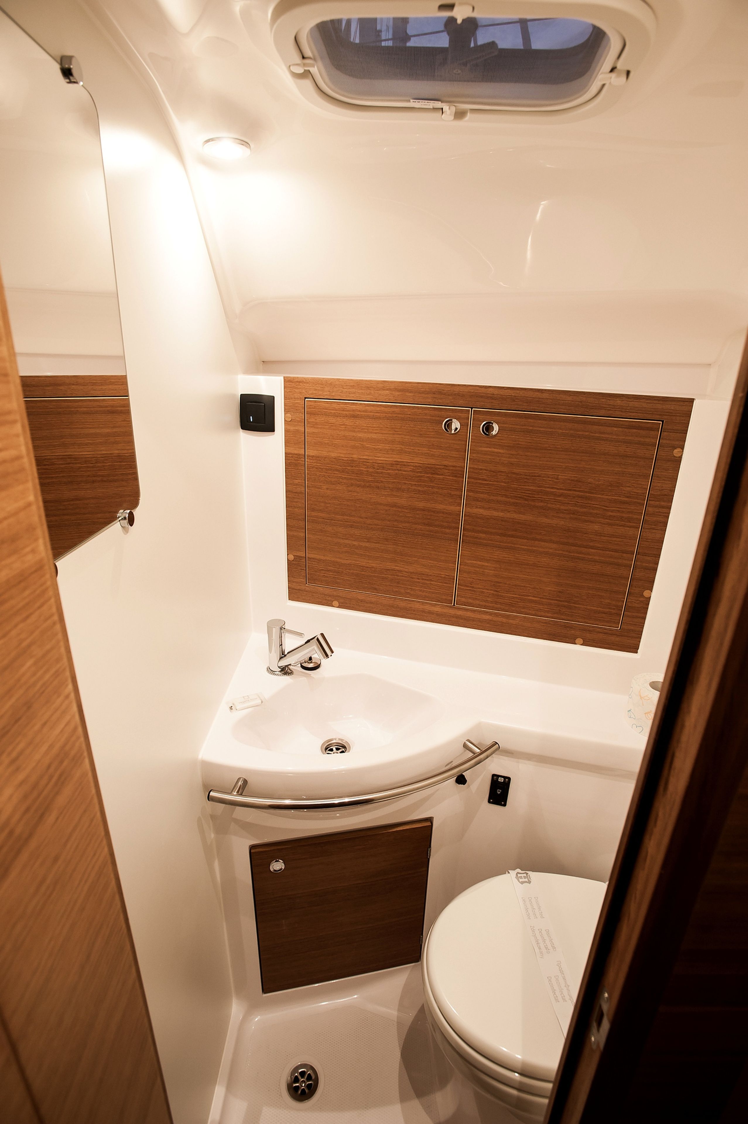 A compact bathroom with a skylight, a sink, a toilet, and wooden cabinetry.