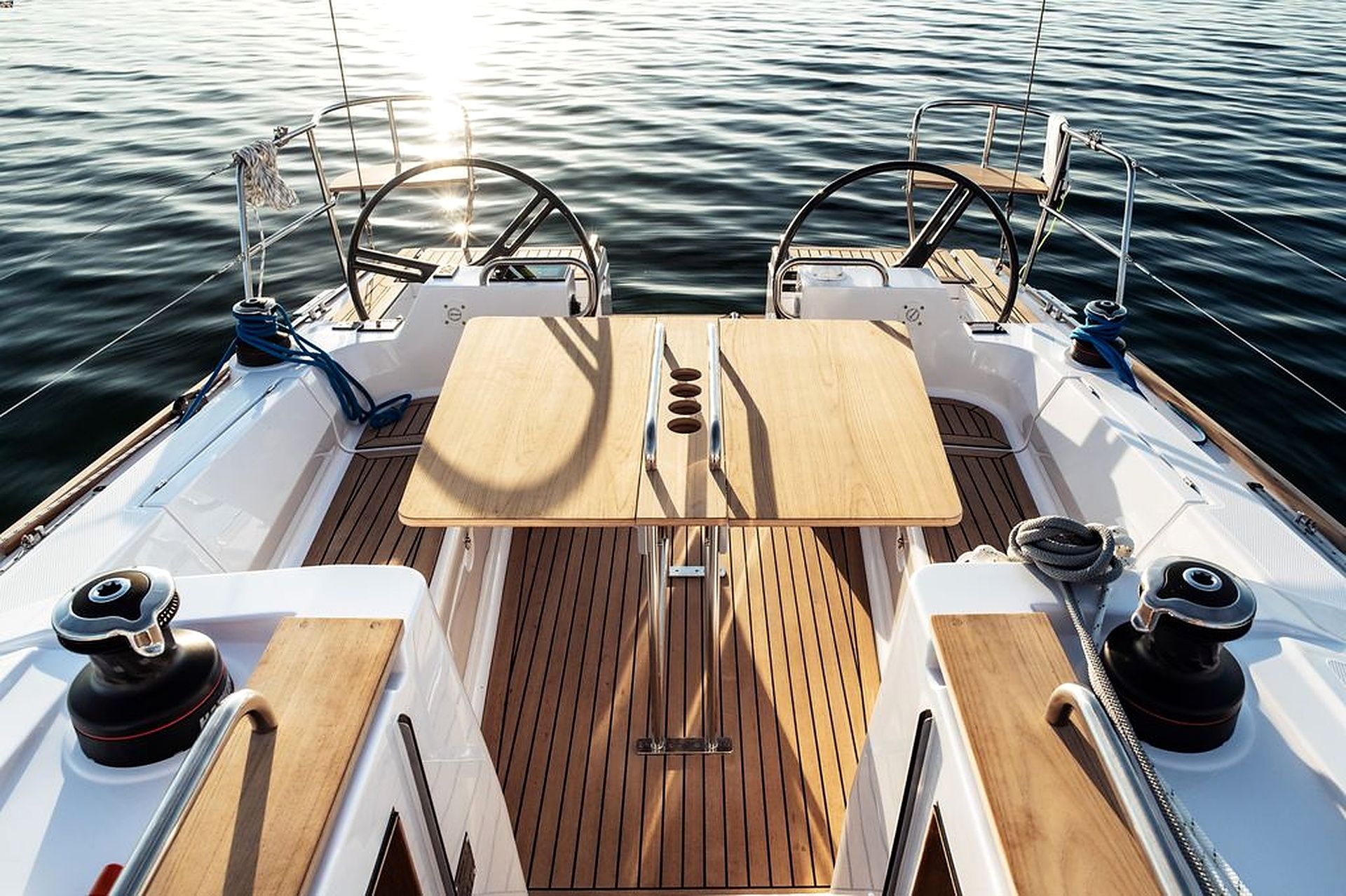 A boat's deck with a central table, two steering wheels, and a rope coiled on the side.