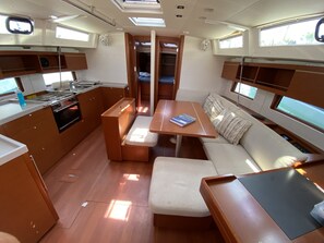 A compact kitchen with a stove, sink, and storage cabinets. There is a dining area with a table and benches, and a small seating area with cushions. - Sun-Kissed Sailing Adventure in the Dodecanese Islands (Kos)