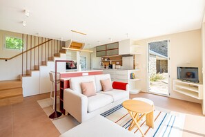A modern living space with a staircase, a sofa, a dining area, a kitchen, and a television. - Le Petit Rivage - Proche de la plage (Sarzeau)