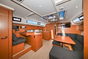 Eine kleine Kombüse mit Spüle, Herd und Bedienfeld; ein Essbereich mit Tisch und gepolsterten Sitzgelegenheiten; und eine weitere kleine Kombüse mit Kühlschrank und Mikrowelle.