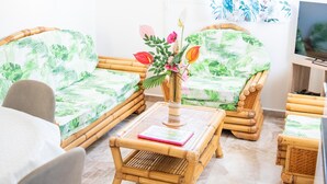 Una stanza con due divani in vimini decorati con motivi a foglia verde, un tavolino con un vaso di fiori e un televisore su un supporto in legno.