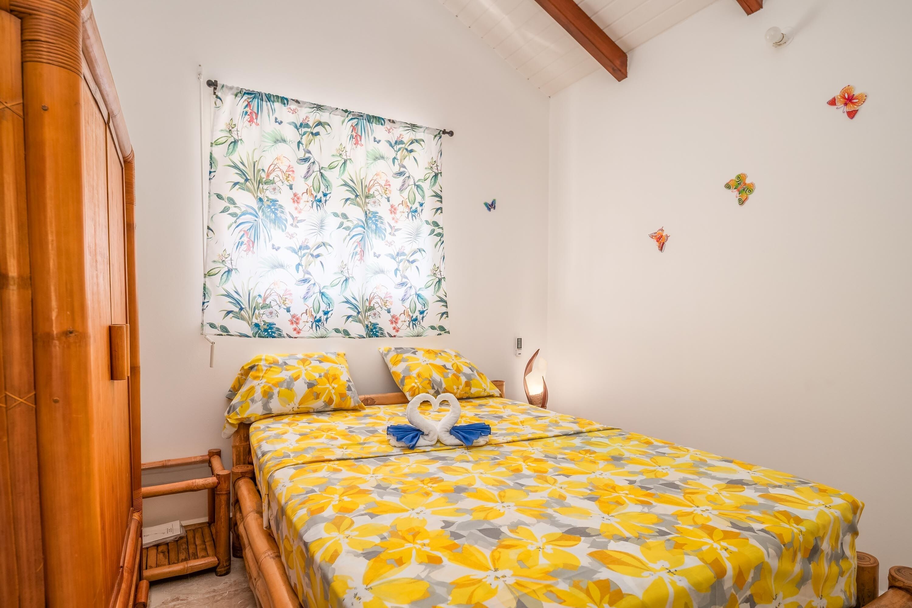 Une chambre comprenant un lit, une armoire en bois, une tapisserie à motifs floraux et des décorations en forme de papillons fixées au mur.