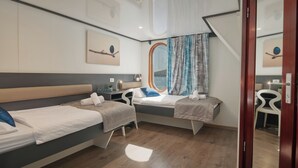 Hotellihuone, jossa on kaksi sänkyä, työpöytä, tuoli, ikkuna verhoilla ja kattovalaisin.