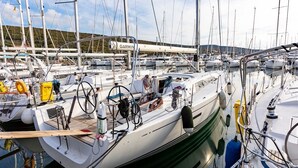 Un puerto deportivo con varios veleros amarrados, un dispositivo de navegación Garmin visible y un paisaje montañoso al fondo.