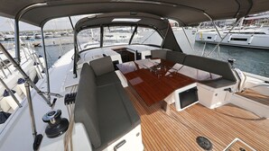 A boat deck with a wooden table, cushioned seating, and a view of other boats in the marina. - Sun-Kissed Sailing Adventure in Zadar, Croatia (Biograd na moru)