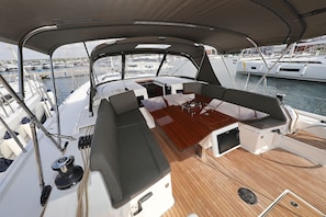 Ein Bootsdeck mit Holztisch, gepolsterten Sitzgelegenheiten und Blick auf andere Boote im Yachthafen.