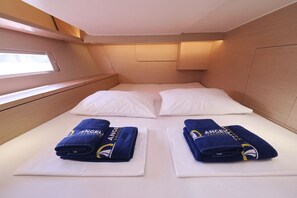 Ein kleines Kabinenzimmer mit Etagenbett, zwei Handtüchern mit einem Logo und einem Fenster für natürliches Licht.