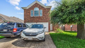 Une allée menant à une résidence, avec un VUS Honda blanc garé devant une maison en briques dotée d’un garage.