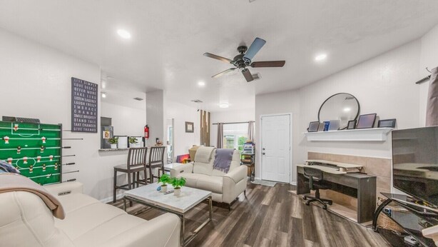 Un salon avec un canapé, une table basse et un baby-foot. On y trouve également un ventilateur de plafond, un téléviseur et une porte qui donne sur une autre pièce.