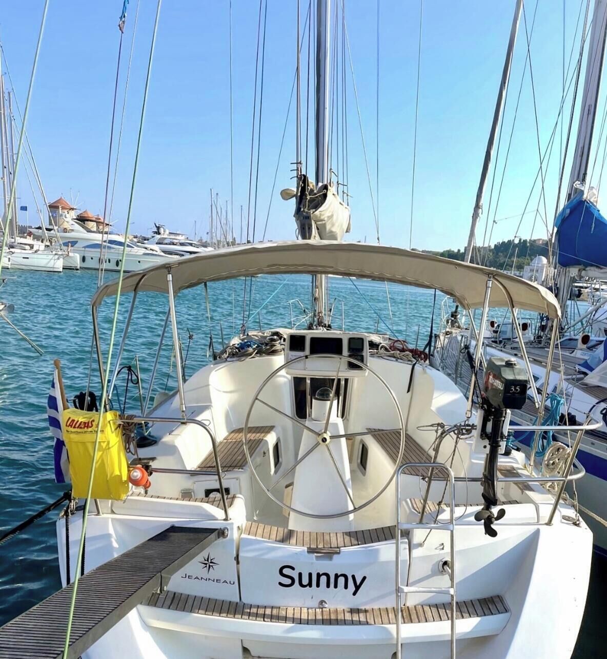 A sailboat named 'Sunny' docked at a marina with other boats in the background.