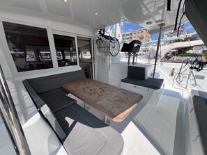 A boat's interior with a wooden table, cushioned seating, and windows offering views of the marina. - Sun-Kissed Sailing Adventure in the Sporades Islands from Volos, Thessaly (Volos)