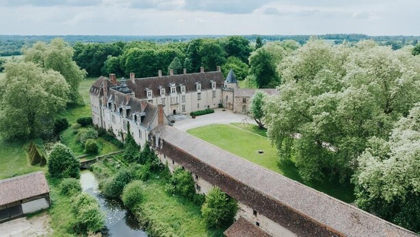A large, historic building with a courtyard, surrounded by lush greenery and a river.