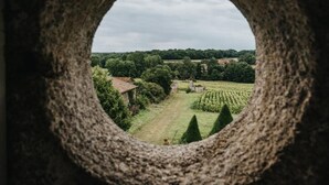A view through a circular opening, revealing a green landscape with trees and a building.