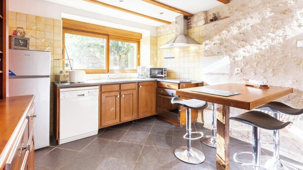 Een moderne keuken met houten kastjes, een vaatwasser, een fornuis en een groot raam.