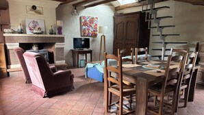 Een eetgedeelte met een houten tafel, stoelen, een open haard, een televisietoestel en een trap.