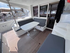 Ein Bootsdeck mit Tisch, Sitzgelegenheit, Mast und Fenstern.