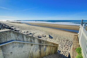 En strand med en betongtrappa som leder ner till strandkanten, en sandstrand och en klarblå himmel.