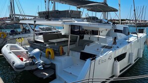 Um iate atracado em uma marina, com área de estar coberta, um barco inflável pequeno e um flutuador.