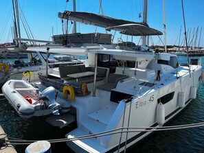 Eine Yacht liegt in einer Marina festgemacht, mit einem überdachten Sitzbereich, einem kleinen Schlauchboot und einem Rettungsring.