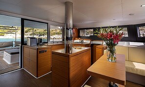 A modern kitchen with wooden cabinetry, a stainless steel range hood, and a view of the sea through large windows.
