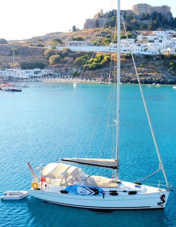 A sailboat docked near a coastal town with white buildings and a castle on a hill.