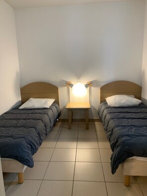 A room with two single beds, a small table with a lamp, and a tiled floor. - South-west-facing flat with a terrace, 1 km from the beach (Ondres)