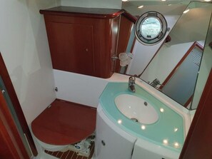 Een compacte badkamer met een houten kastje, een ronde spiegel en een lichtgroene wastafel.