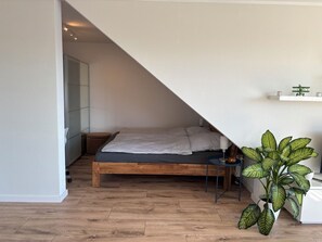 Une chambre avec un plafond en pente, un lit en bois, une table de chevet, une lampe et une plante en pot.