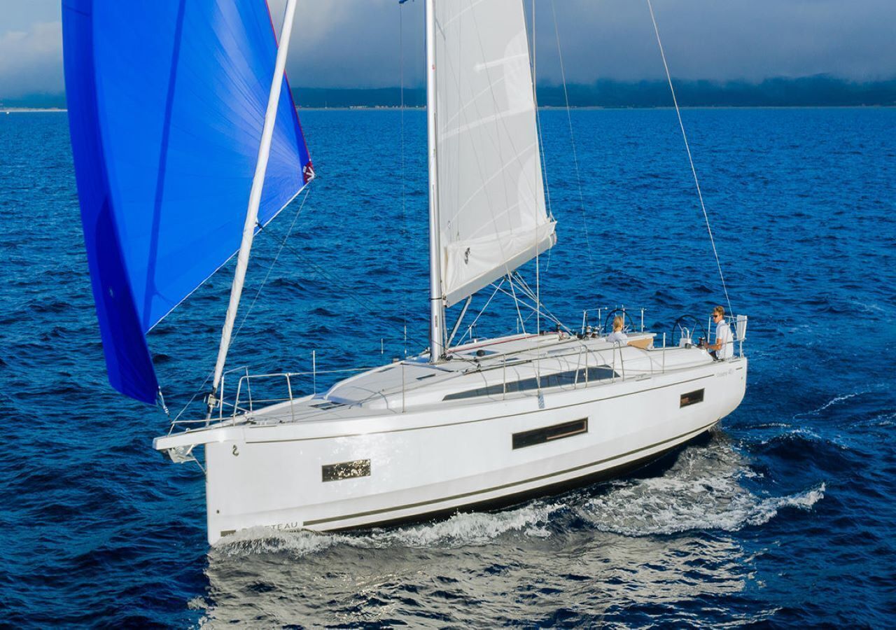 Un voilier blanc avec une voile bleue sur l’eau.