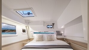 Un dormitori modern a bord d'un iat amb llit, finestra panoràmica i vista al mar.