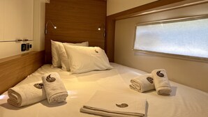 A hotel room with a bed, pillows, a window with blinds, and rolled towels with a leaf design. - Sun-kissed Sailing Adventure in the Ionian Islands (Preveza)