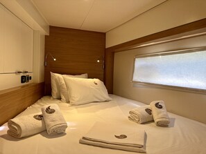 A hotel room with a bed, pillows, a window with blinds, and rolled towels with a leaf design. - Sun-kissed Sailing Adventure in the Ionian Islands (Preveza)