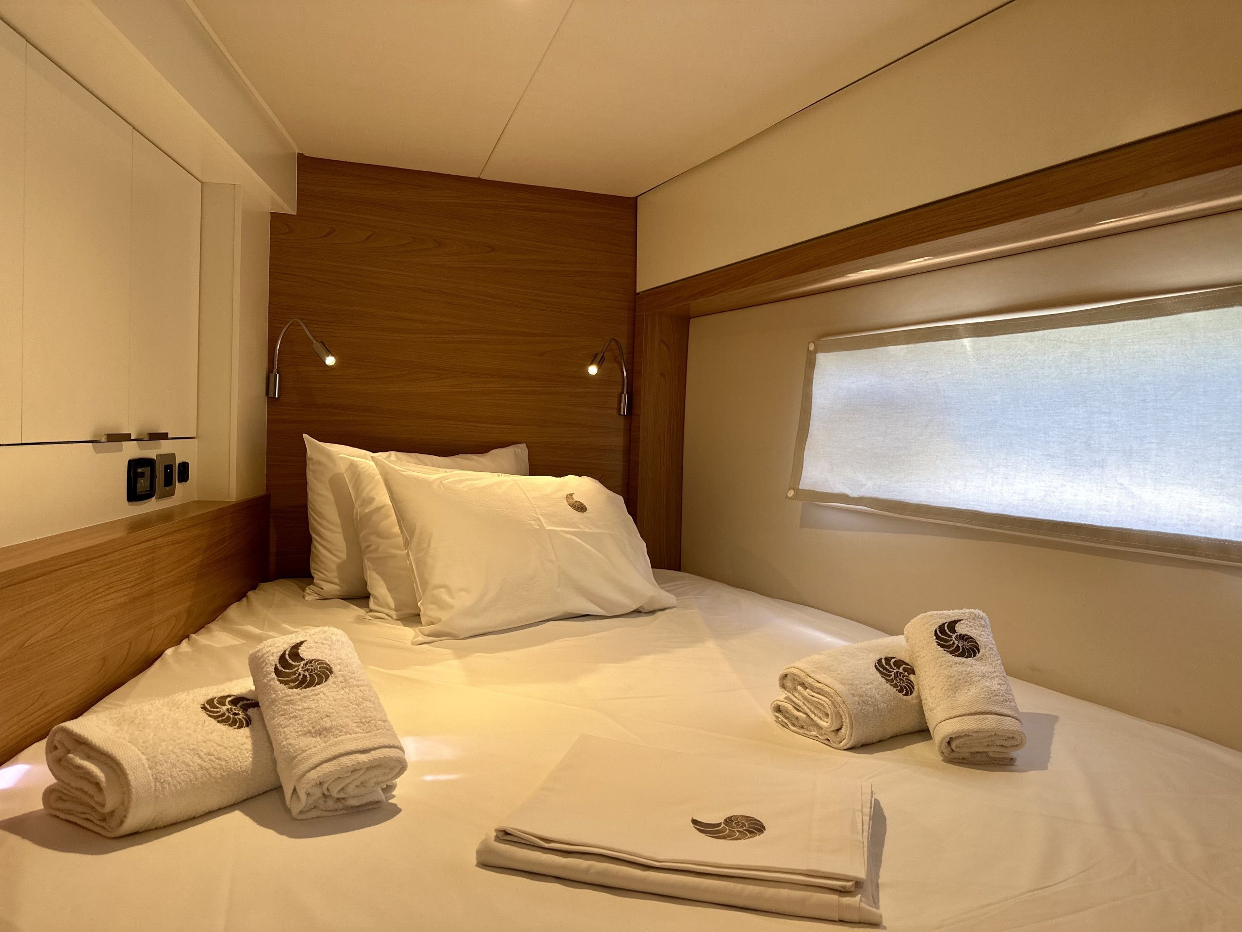 Ein Hotelzimmer mit einem ordentlich bezogenem Bett, einem Fenster mit Jalousien und einem Holzkopfteil.