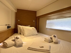 A hotel room with a neatly made bed, a window with blinds, and a wooden headboard. - Sun-kissed Sailing Adventure in the Ionian Islands (Preveza)