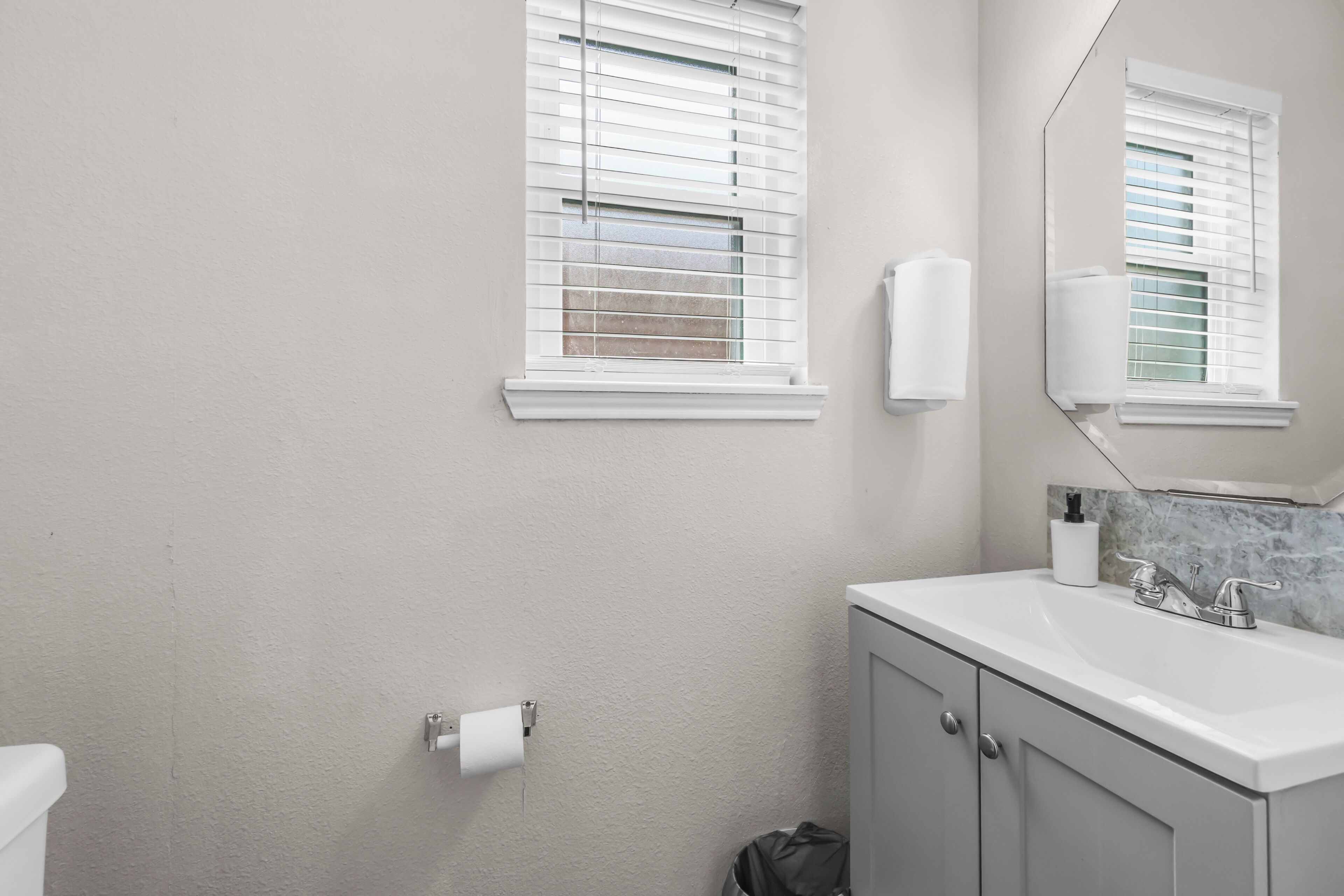 Une salle de bain équipée de toilettes, d’un lavabo, d’un miroir et de stores aux fenêtres.
