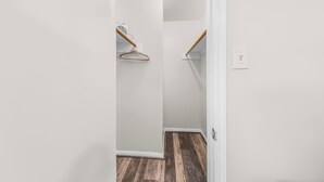 Un pasillo estrecho con suelo de madera, una pared blanca y una puerta que da a otra habitación.