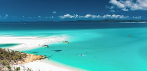 A coastal landscape with clear turquoise waters, a sandy beach, and boats.