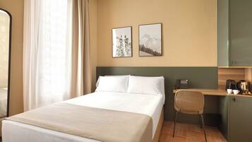 A hotel room with a bed, a desk with a phone and coffee maker, and two framed pictures on the wall.