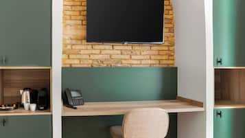 Een kamer met een bakstenen muur, een wandgemonteerde flatscreen-tv, een houten bureau, een rieten stoel en een koffiezetapparaat.