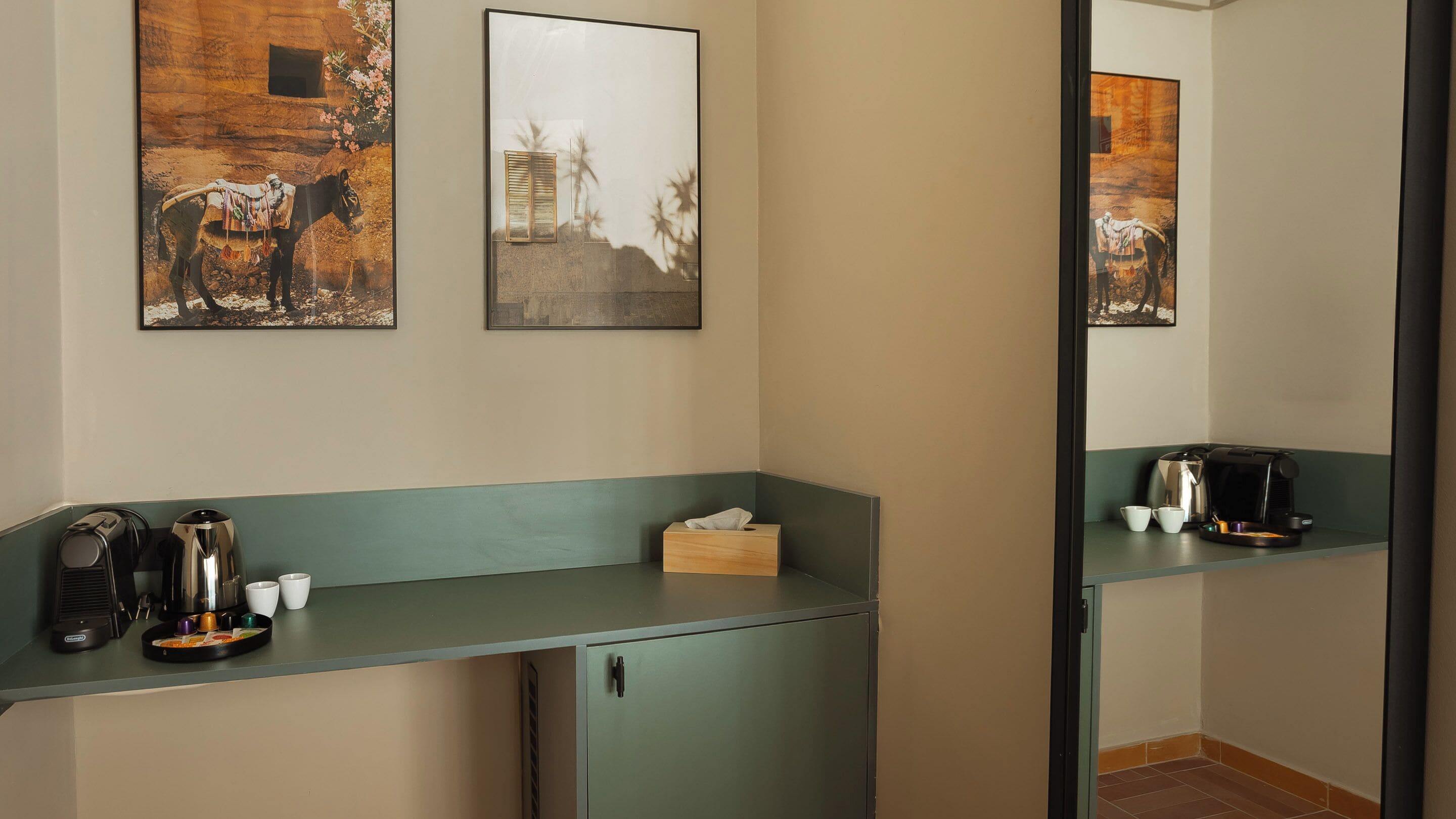 A hotel room with a kitchenette, a mirror, and artwork on the wall.