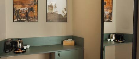 A hotel room with a kitchenette, a mirror, and artwork on the wall.