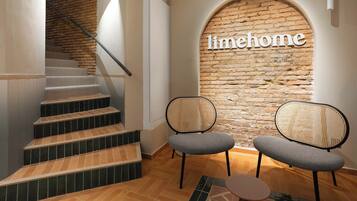 A staircase leading to a room with a brick wall and the word 'limehome' on it. There are two chairs and a small table in the room.